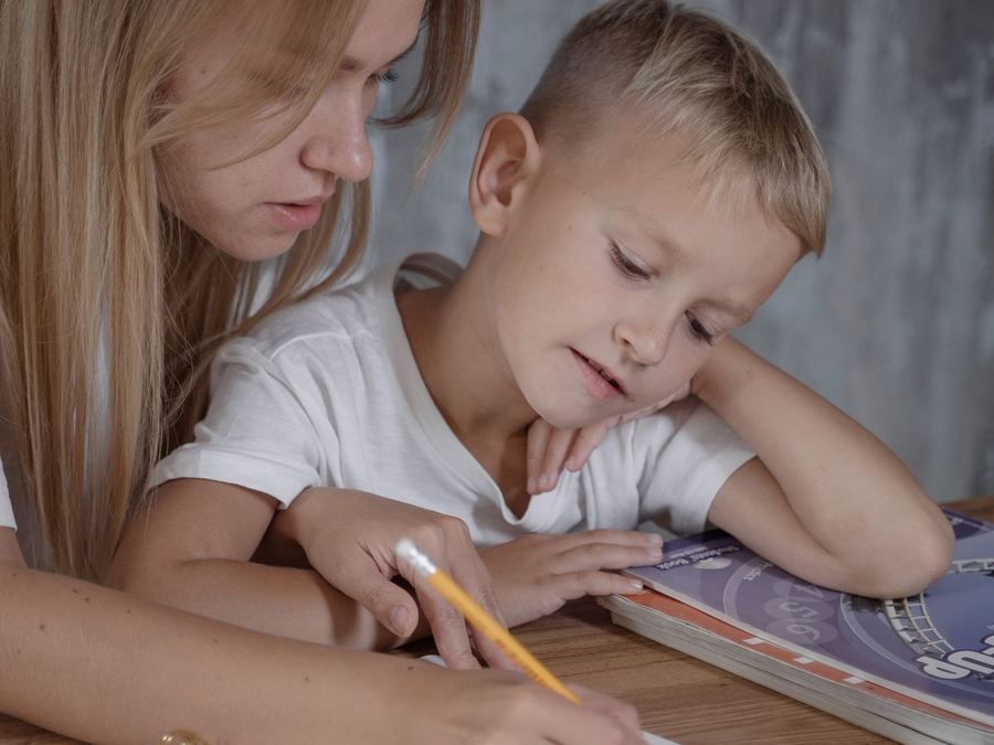 An adult and a young child working through a notebook together at a table at home