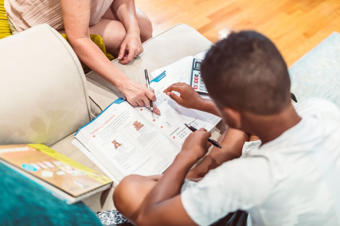 A tutor pointing at a workbook page while a primary school student writes at a table