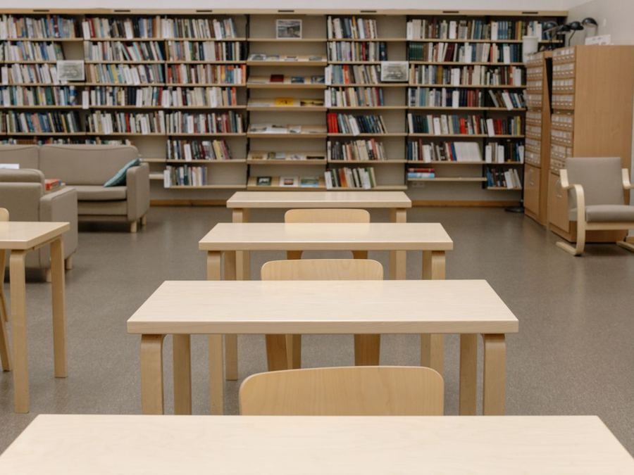 Empty wooden study tables in a local library, with full bookshelves along the wall